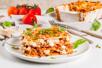 Italian food recipe. Dinner with classic lasagna bolognese with béchamel sauce, parmesan cheese, basil and tomatoes, on white marble table, coopy space