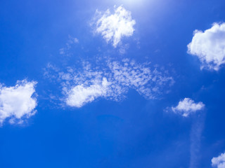 White fluffy clouds in the bright blue sky with light from the Sun