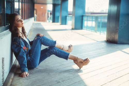 Zdjęcie XXL piękna dziewczyna siedzi na podłodze dworca kolejowego. młoda kobieta w dżinsowe ubrania siedzi na ulicy. skopiuj miejsce na Twój tekst