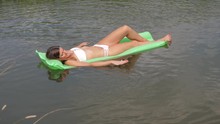 Young Tanned Woman In A White Bikini Floating In The River On The Mattress.