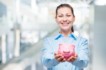 Happy woman holds a piggy bank full of money, photo in office