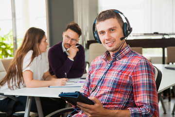 Wall Mural - Young man in headphones and microphone with collegues in office