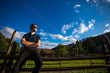 © Svetlana - A young happy handsome man in sunglasses resting on a wooden handmade fence in garden with a chic mountain view