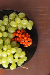 Green grapes, blue plums and orange rowan berries on a black plate for designer in retro style