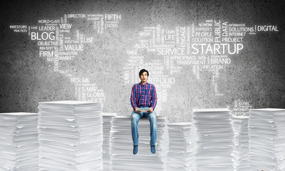 Attractive man sitting on pile of paper documents.