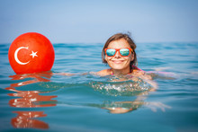 Young Girl Swims In Blue Water At Sea With A Turkish Flag Depicted On A Balloon. Sea Beach Vacation In Turkey. Smiling Girl On Sea.