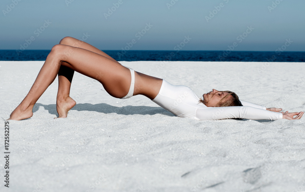 Beautiful tanned woman in a white swimsuit on the beach. - obrazy, fototapety, plakaty 