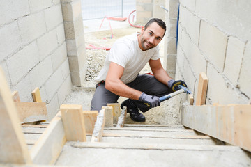 Wall Mural - young man mason demolding concrete stairs with hammer in a new house construction site