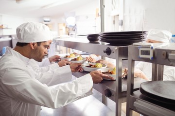 Chefs passing ready food to waiter at order station