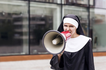 Surprised nun speak to megaphone outdoors.