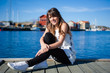 © vladteodor - Young and happy tourist woman sitting in the harbor on wood pier