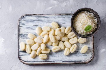 Wall Mural - Raw uncooked potato gnocchi on white wooden chopping board with ingredients. Flour, grated parmesan cheese, basil over gray concrete background. Top view with space. Home cooking.