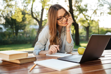 Poster - Pleased brunette woman in eyeglasses sitting by table