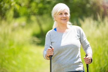 Canvas Print - Senior woman nordic walking in park
