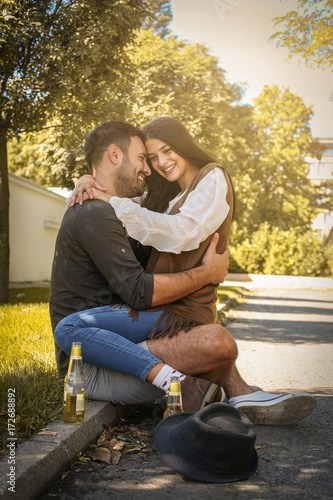Young Couple Sitting In Park And Holding Bottle Of Drink Girlfriend