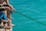Fototapeta Tęcza - Children are fishing on the pier. Close-up of hands and rods