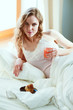 © lenets_tan - Young woman drinking cup of coffee or tea while lying in bed.