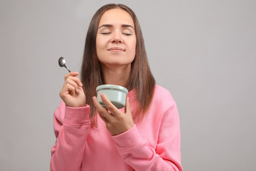 Young woman eating yogurt on light background