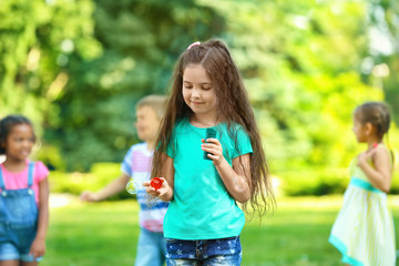 Wall Mural - Cute little girl blowing soap bubbles outdoors