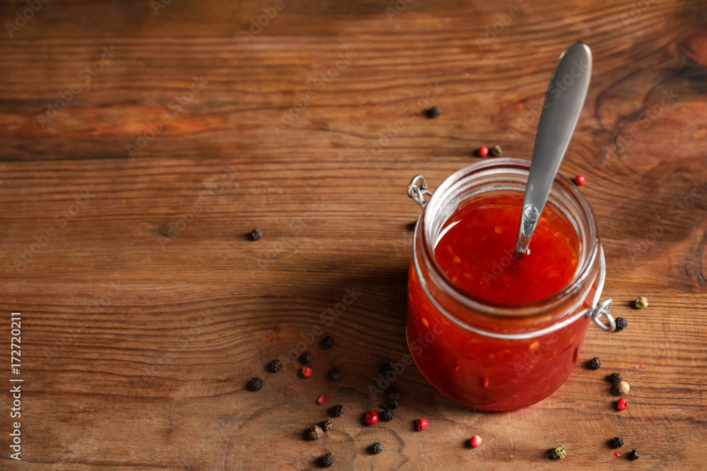 Glass jar with chili sauce on wooden background