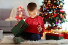 Cute Little Boy Opening Gift Box In Room Decorated For Christmas