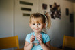 © Jessica Byrum/Stocksy - Toddler girl with pigtails sitting on the kitchen table drinking a big glass of water.