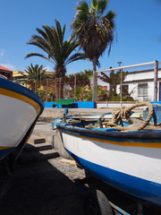 two small fishing boats on the harbor at puerto de la cruz tenerife with dockside rope palm trees and blue sky