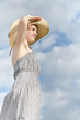 Beautiful girl in hat and dress looking afar against a cloudy blue sky background