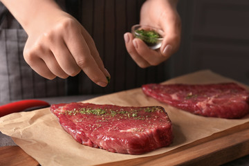 Wall Mural - Woman adding spices to raw steak on kitchen table