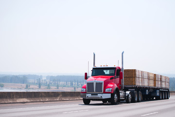 Wall Mural - Big rig day cab red semi truck with flat bed trailer transporting lumber wood by wide multiline highway