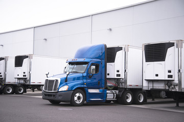 Big rig day cab semi truck and reefer trailers with refrigerator units loading cargo from warehouse building