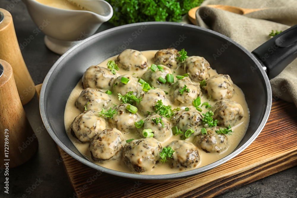 Frying pan with delicious meatballs in sauce on table