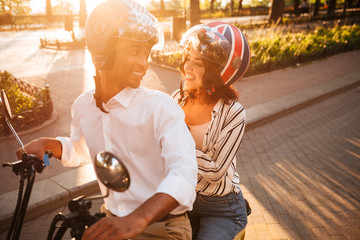 Happy african couple rides on modern motorbike in park