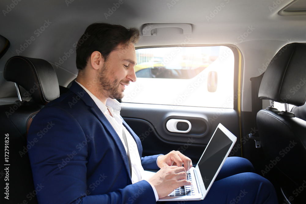 Handsome man with laptop sitting in taxi car