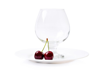 Empty cognac glass next to cherry berries on a white plate isolated on white background