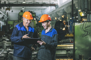 two workers at an industrial plant with a tablet in hand, working together manufacturing activities