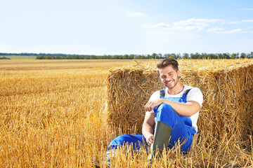 Sticker - Young male farmer sitting near pressed straw briquette in field