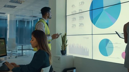 Business team looking at large video screen and computers with charts and data