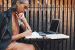 © Studio Firma/Stocksy - Smiling mature woman writing in notebook at wooden table outdoors