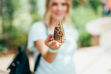Brown Butterfly Resting On Fingertip Of Young Blonde Woman
