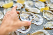Open oyster in a male hand, against the background of open oyste