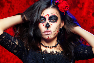 Closeup halloween style portrait of beautiful woman with facial art - traditional mexican skull at red background.