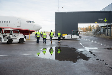 Workers Walking Towards Airplane On Wet Runway