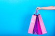 © mirage_studio - Female hand holding colorful shopping bags isolated on blue (cyan) background, free space, close up. Sale, consumerism, advertisement and black friday concept. Closeup of colored paper shopping bags