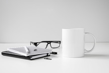 Black And White Coffee Mug Mock Up With Notebooks, Pen And Glasses On Work Desk.