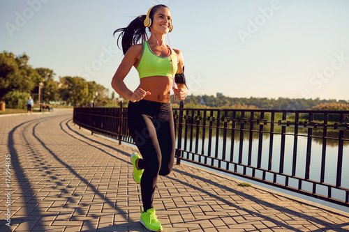 Plakat Dziewczyna sportowa w słuchawkach biegnie przez park. Zdrowy tryb życia.