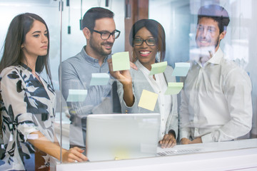 Wall Mural - Creative business people discussing in front of glass wall using sticky notes.