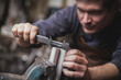 © Gonzales Photo - A blacksmith is taking measures on a piece of metal in a workshop.