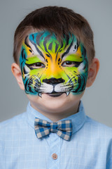 little boy painted like a tiger on a gray background. face painting