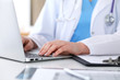 © rogerphoto - Close up of unknown female doctor typing on laptop computer while sitting  at the table